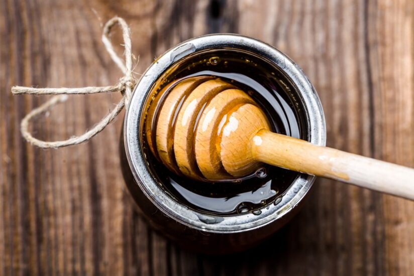 Glass jar of honey and dipper in honey on rustic wooden background